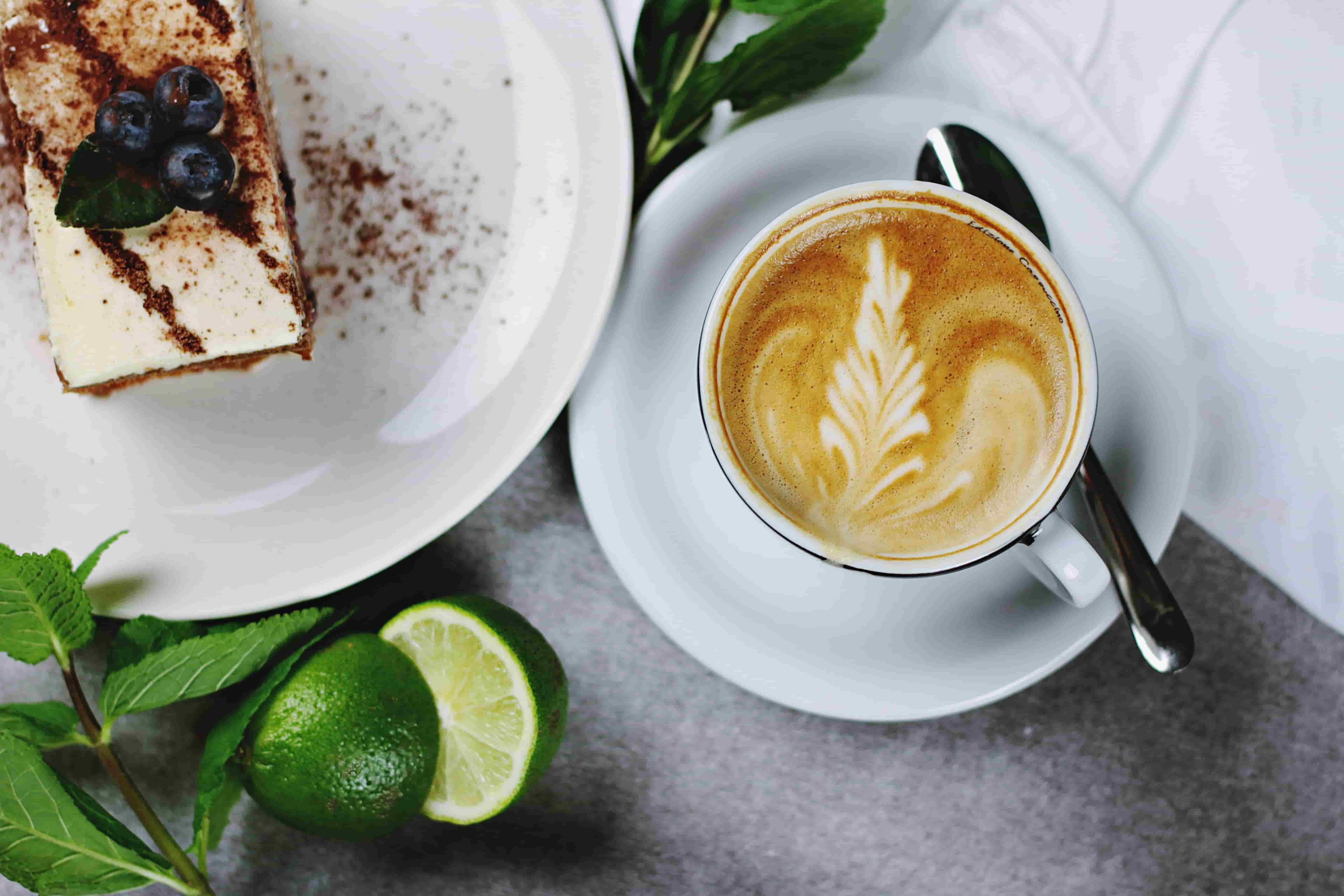A cup of coffee, a slice of cake and some decorative limes.