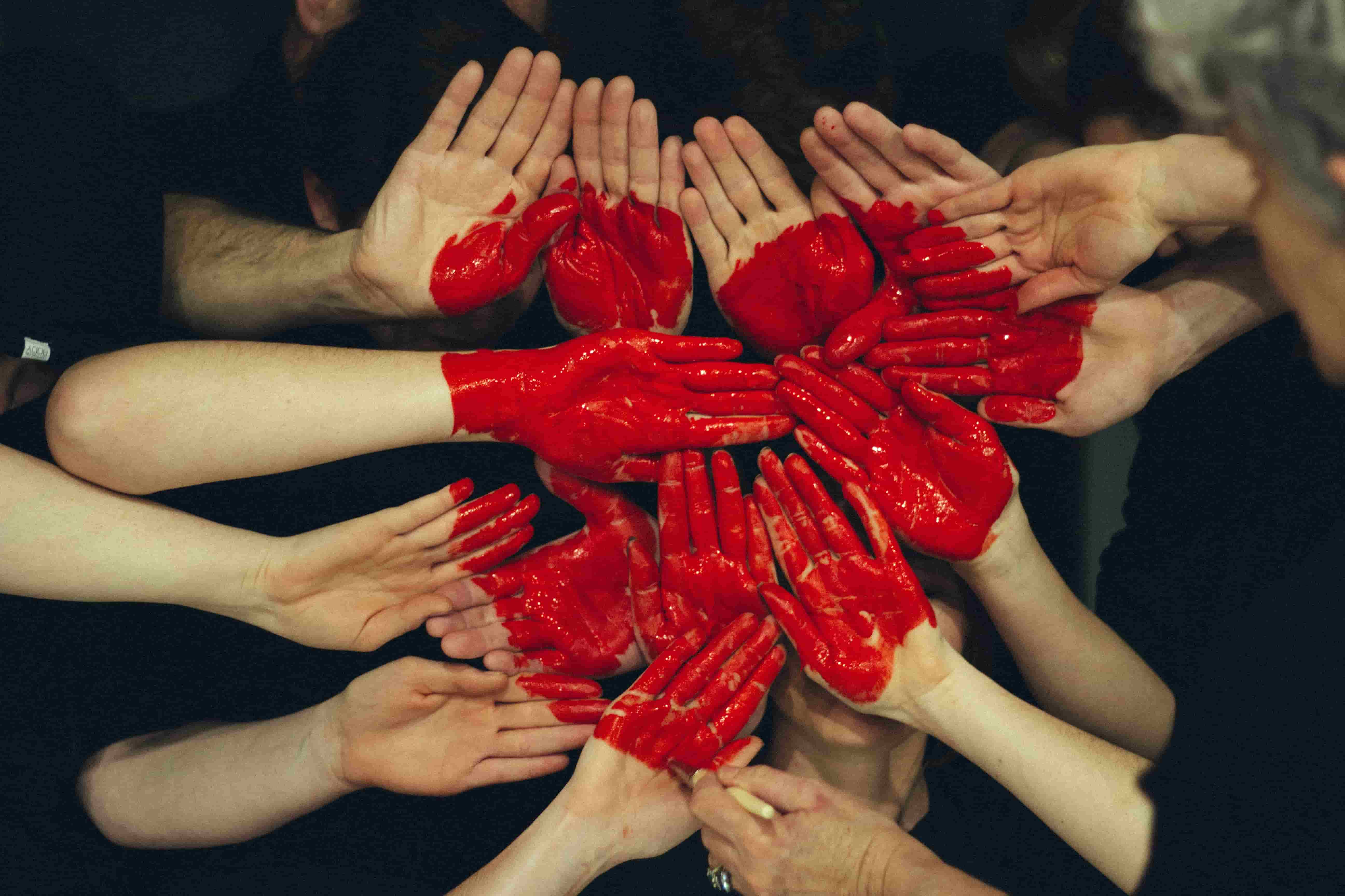 A close up view of lots of hands with palms facing upwith a large red heart painted onto the hands. 