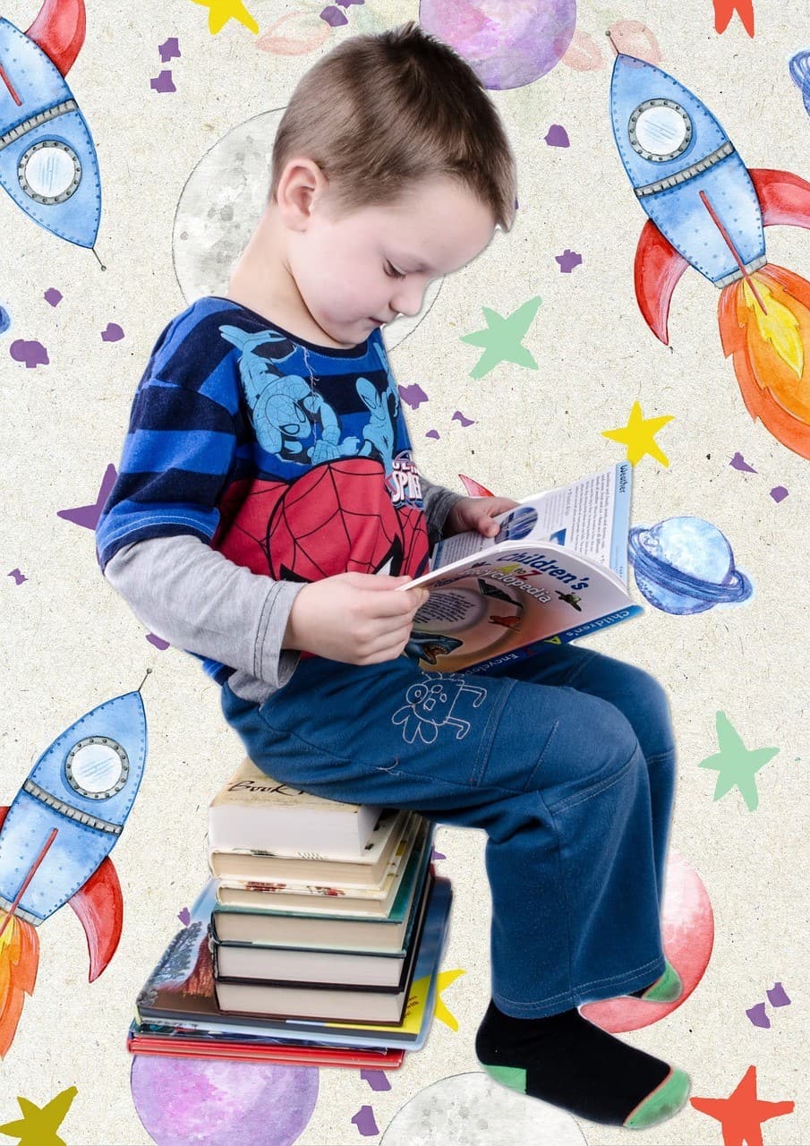 A young boy sitting on a stack of books reading a book, with a fun rocket ship background.